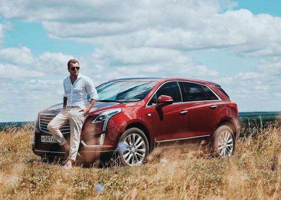 Евгений Фист рядом с Cadillac XT5 на фоне поля
