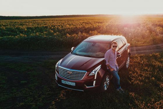 Евгений Фист рядом с красным Cadillac XT5 на фоне заката