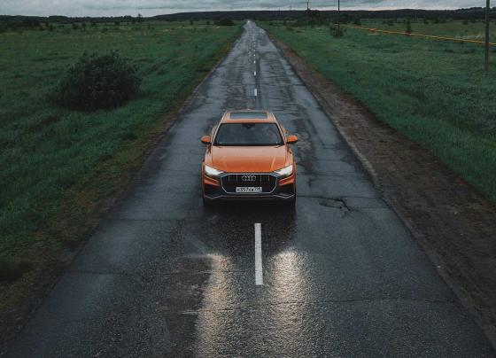 Audi Q8 едет по пустой дороге по мокрому асфальту 